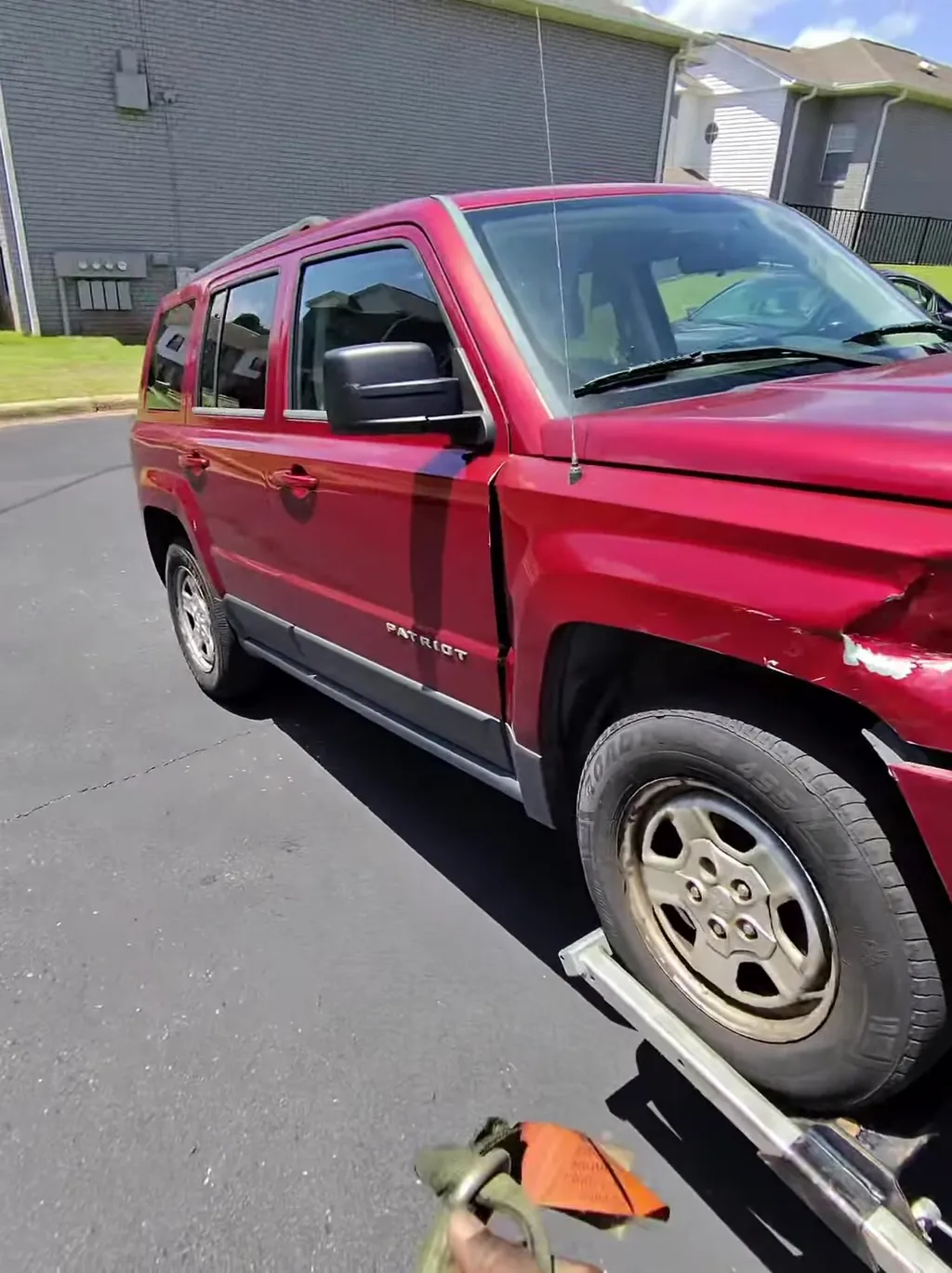 A damaged Jeep Patriot winched onto the deck from an apartment complex lot.