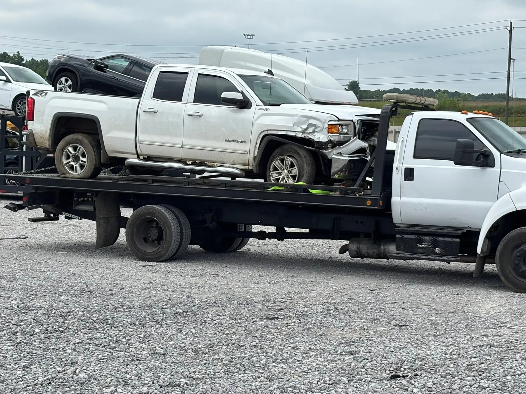 Alexander and Sons Towing rollback loaded with a pickup at a yard